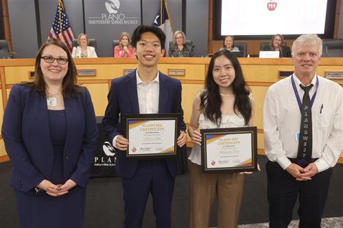 four individuals smiling, the middle two have recognition certificates